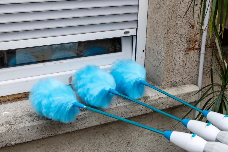 Das Bild zeigt drei blaue Staubwedel, an einem Fenster mit heruntergelassenen Rollläden.