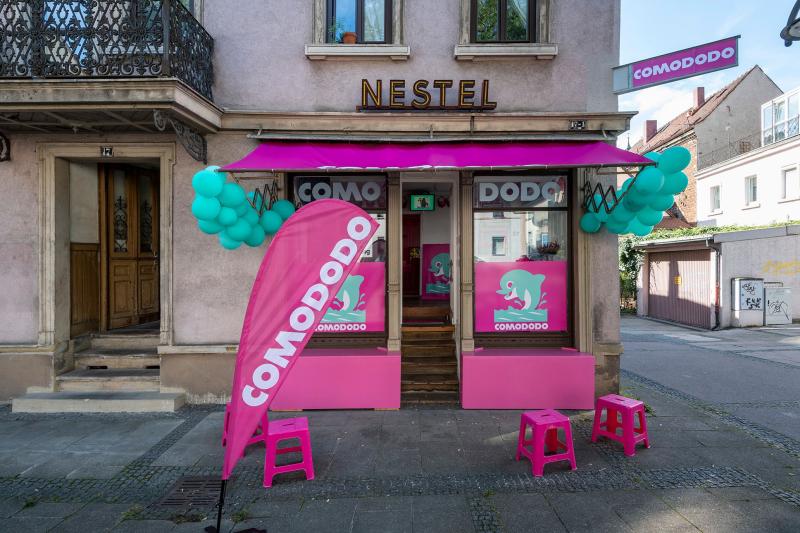 Das Bild zeigt den bunten Eingang eines Lieferdienst für immaterielle Güter, eröffnete während des Festival CURRENT 2023 namens „COMODODO“ mit pinken und türkisfarbenen Dekorationen