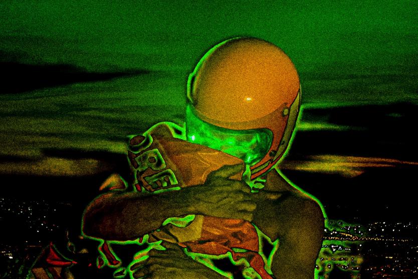 The image shows a person wearing an orange helmet and a bright green visor, tightly hugging an orange package, against a distorted, green-tinted nighttime cityscape.