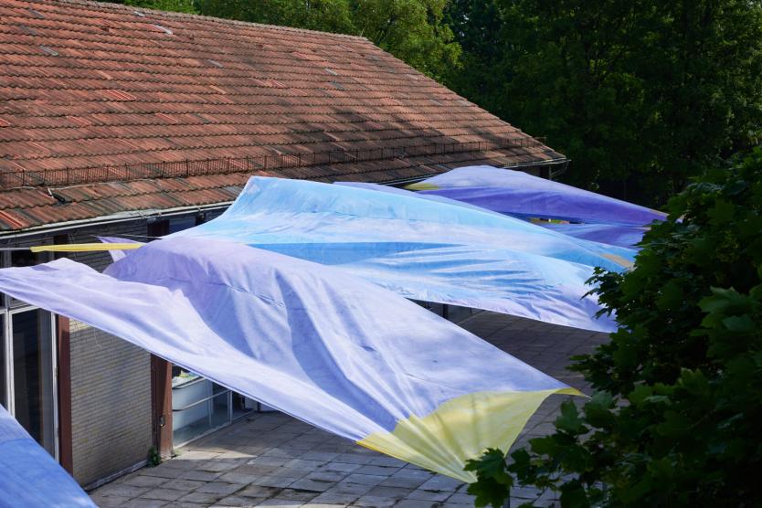 The image shows colorful fabrics attached between a roof and a tree.