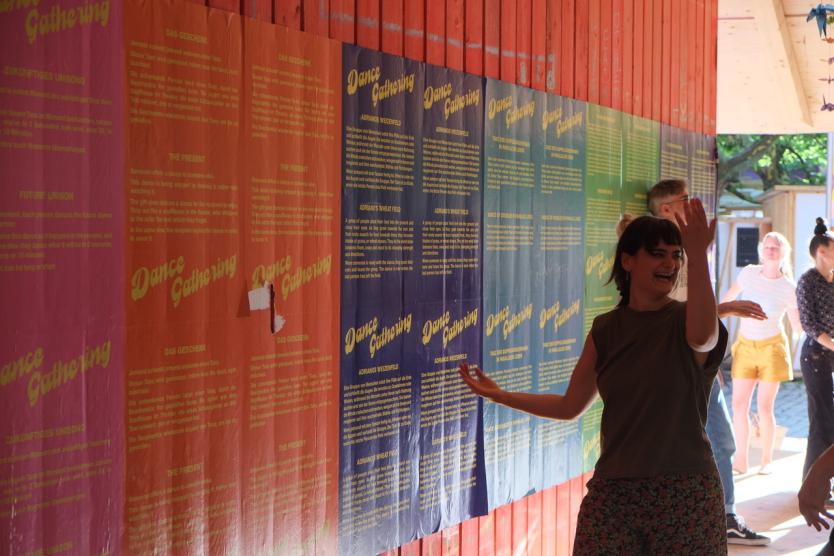 Dancing people in front of a colored wall with posters by „Dance Gathering“