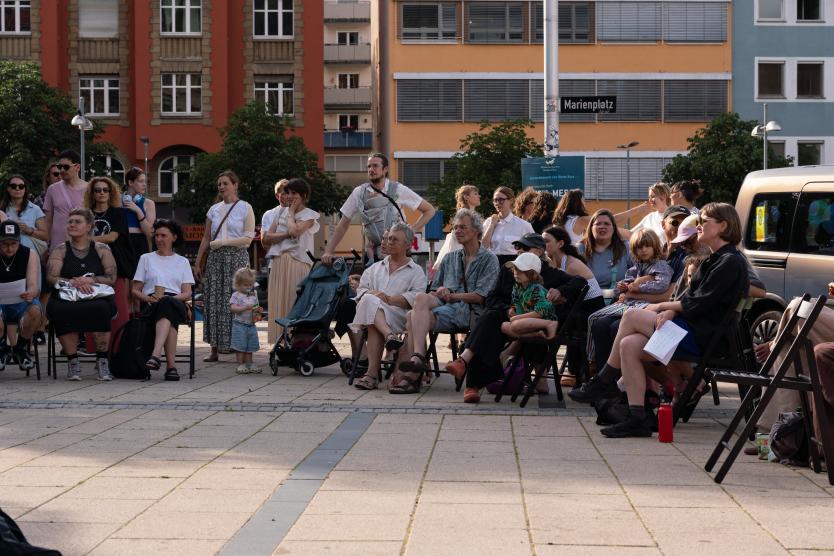 Eine Gruppe von Zuschauenden, stehend und sitzend im Halbkreis.
